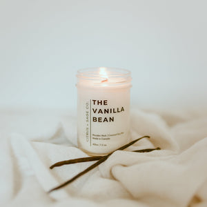 candle on white sheet with vanilla bean in front
