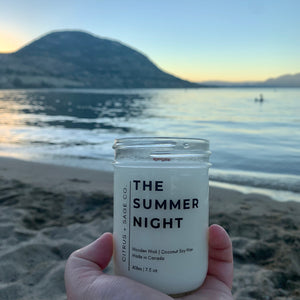 hand holding a candle in a mason jar with the lake and mountains behind