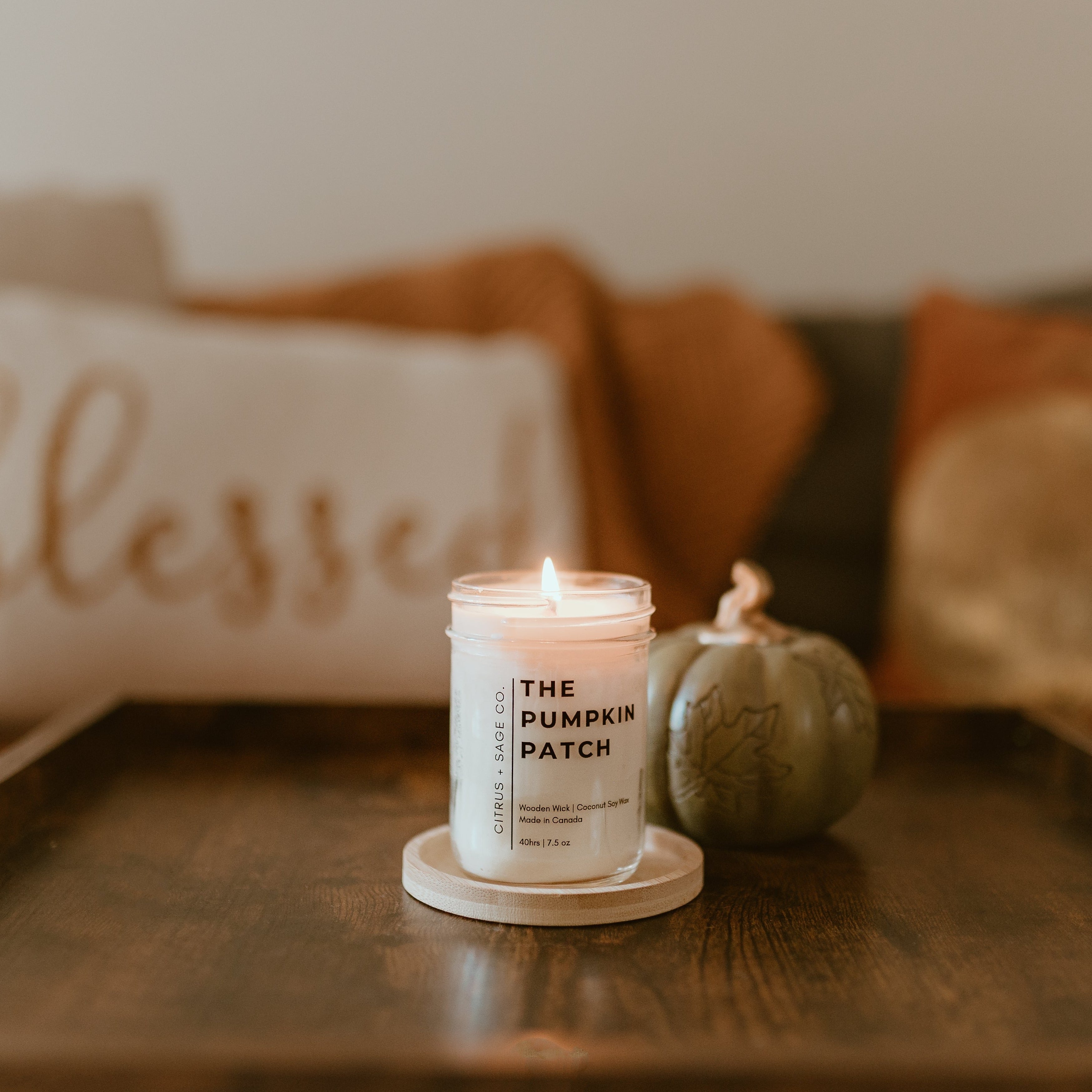 candle with pumpkins & pillows in background